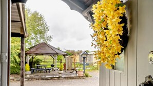 Udsigt gennem en dør med en hængende, gul blomsterdekoration, en trækonstruktion i baggrunden og en grussti.