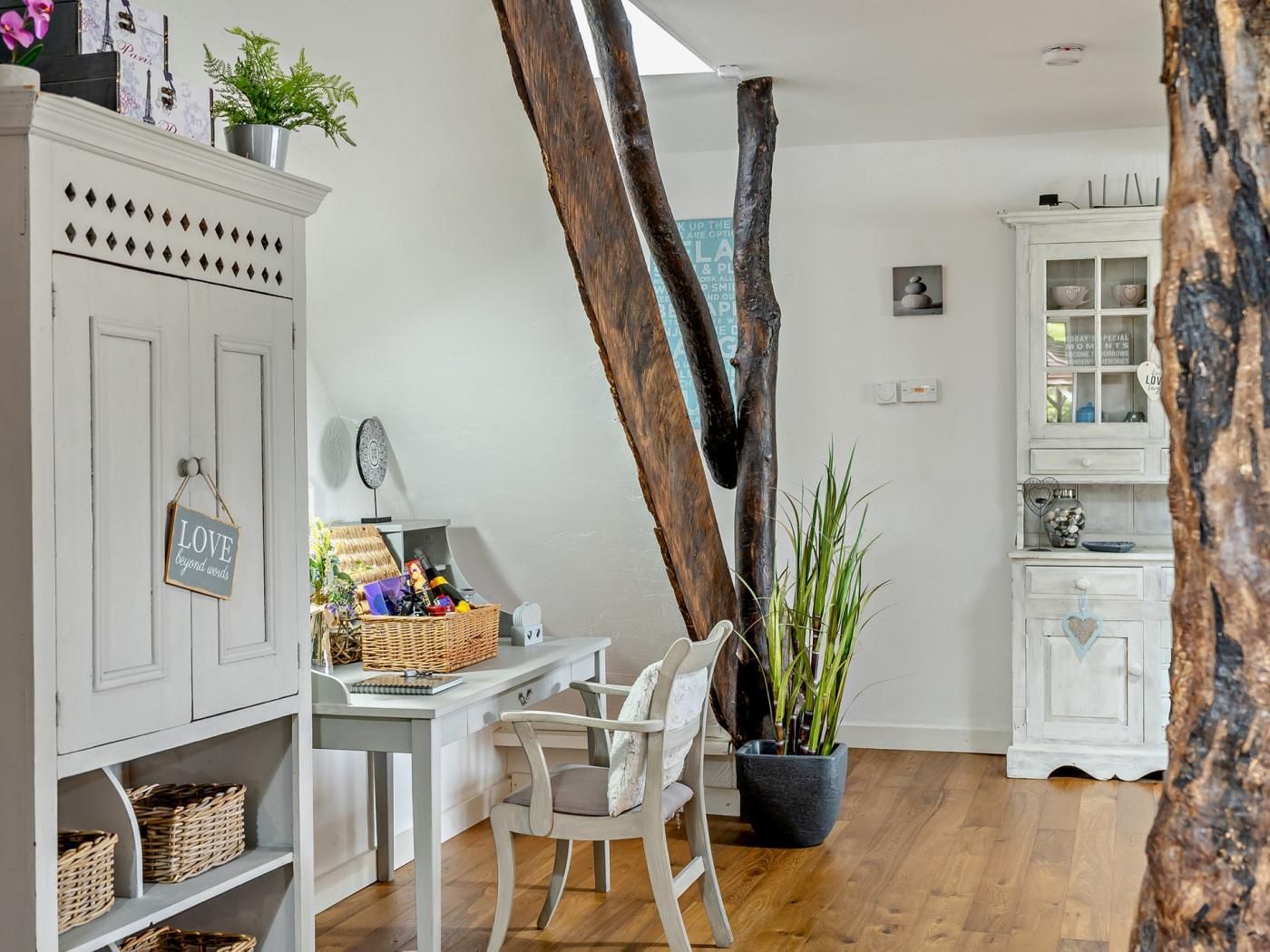 Une pièce comprenant un bureau en bois, une chaise, un meuble avec des paniers et un grand tronc d’arbre.