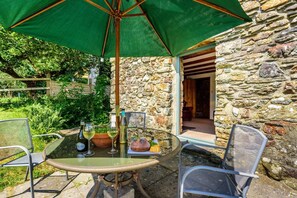 An outdoor patio with a round table, two chairs, a green umbrella, and a stone wall backdrop. - 2 Bed in Newport (oc-78803) (Llwyngwair Manor)
