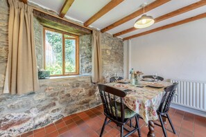 A dining area with a stone wall, wooden beams, a window with curtains, and a table set for two with chairs. - 2 Bed in Newport (oc-78803) (Llwyngwair Manor)