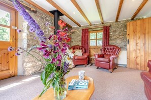 A cozy room with stone walls, wooden beams, a fireplace, leather chairs, and a vase of flowers on a table. - 2 Bed in Newport (oc-78803) (Llwyngwair Manor)