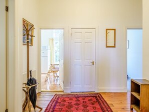 A hallway with a wooden floor, a red patterned rug, a white door, and a wooden bench. - 3 Bed in Edinburgh (oc-79008) (Edinburgh)