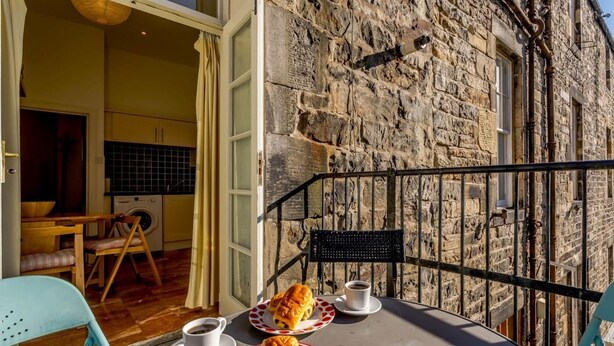 A stone building with a balcony, a table with plates of pastries and cups, and a chair. - 3 Bed in Edinburgh (oc-79008) (Edinburgh)