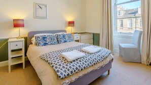 A bedroom with a bed, two bedside lamps, a chair, a window with curtains, and a wall-mounted picture. - 3 Bed in Edinburgh (oc-79008) (Edinburgh)