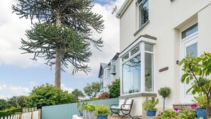 Il s’agit d’une propriété résidentielle dotée d’un grand arbre, d’une clôture bleue et d’un mur blanc percé d’une fenêtre.