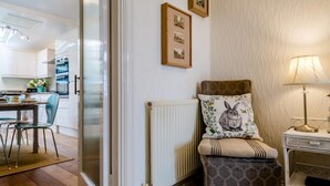 Une cuisine moderne avec des meubles blancs, un coin repas comprenant une table et des chaises, un radiateur et un mur orné de tableaux encadrés.