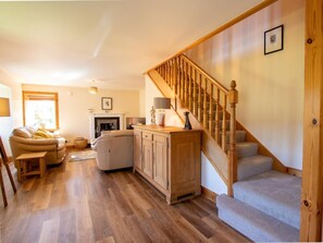 A living room with a fireplace, sofa, and wooden staircase. - 3 Bed in Pitlochry (oc-78841) (Dalchalloch)