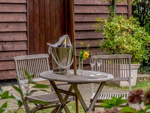 An outdoor wooden table with a metal bucket, a vase with flowers, and two wine glasses.