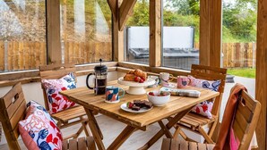 Ein Holztisch mit Stühlen, einer Kaffeekanne und einem Teller Essen.