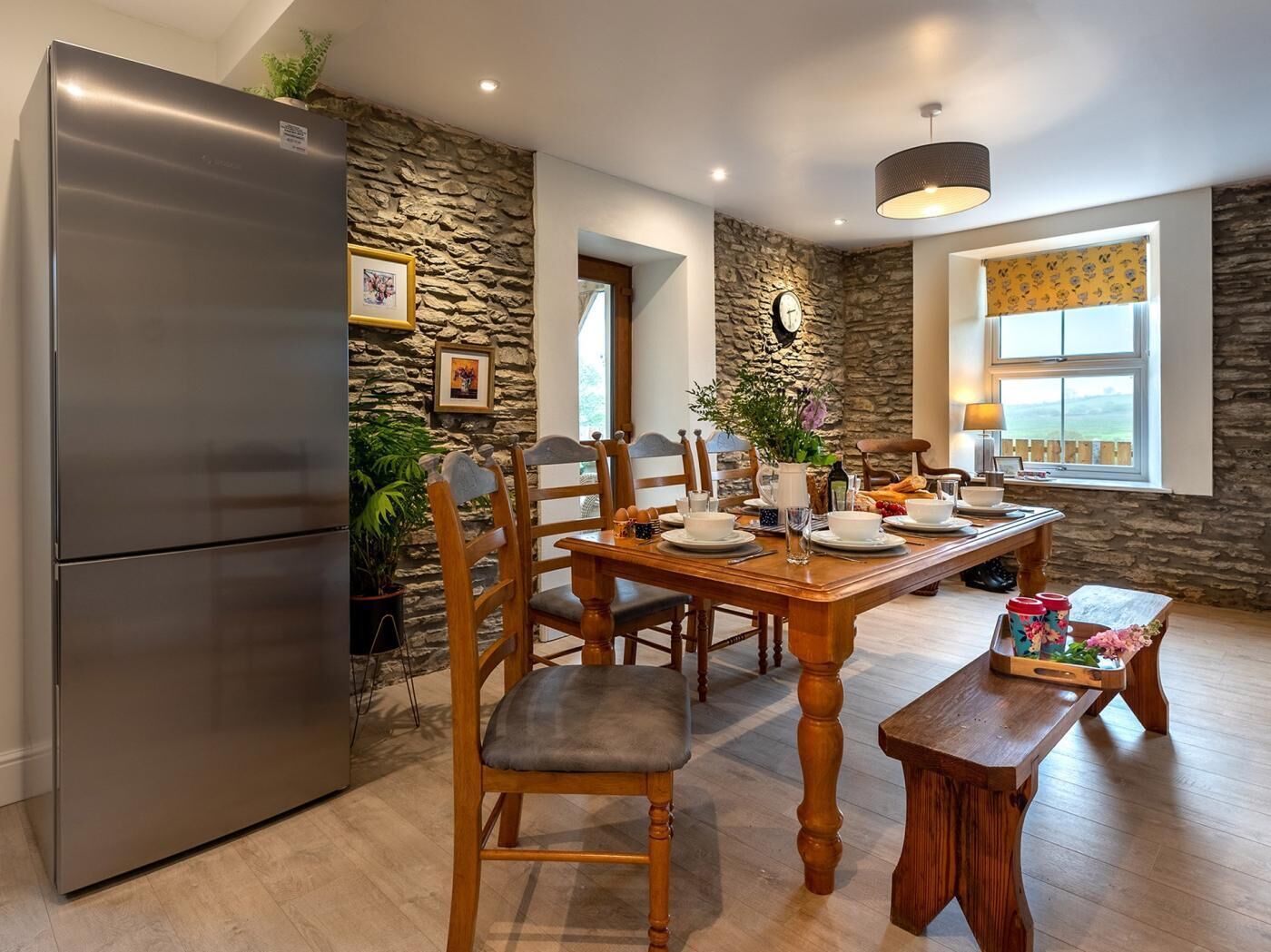 Une cuisine moderne dotée d’un réfrigérateur encastré en acier inoxydable, d’une table à manger en bois, de murs décoratifs en pierre et d’une grande fenêtre offrant une vue imprenable.