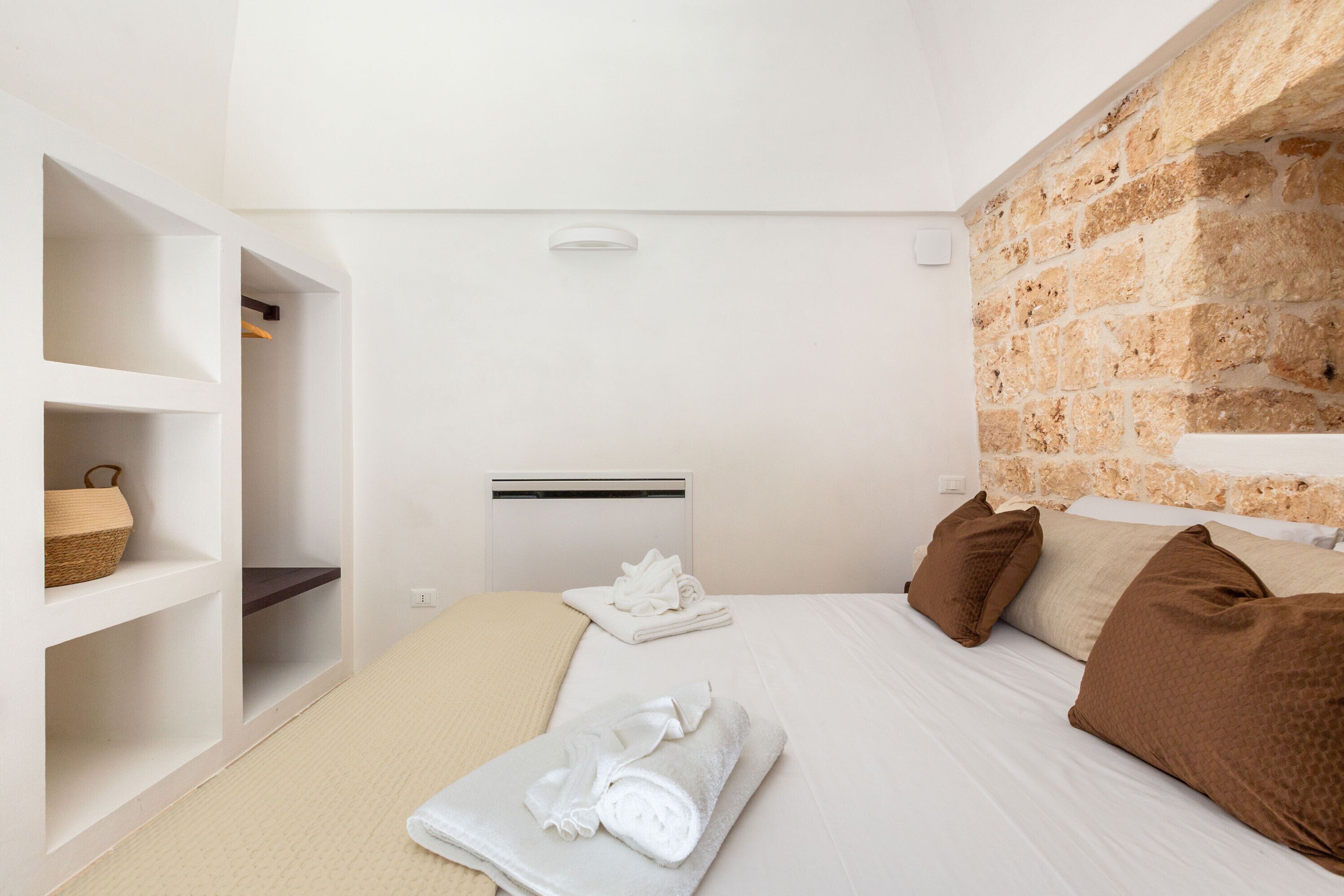 A hotel room with a bed, a wardrobe, a brick wall, and a ceiling vent.