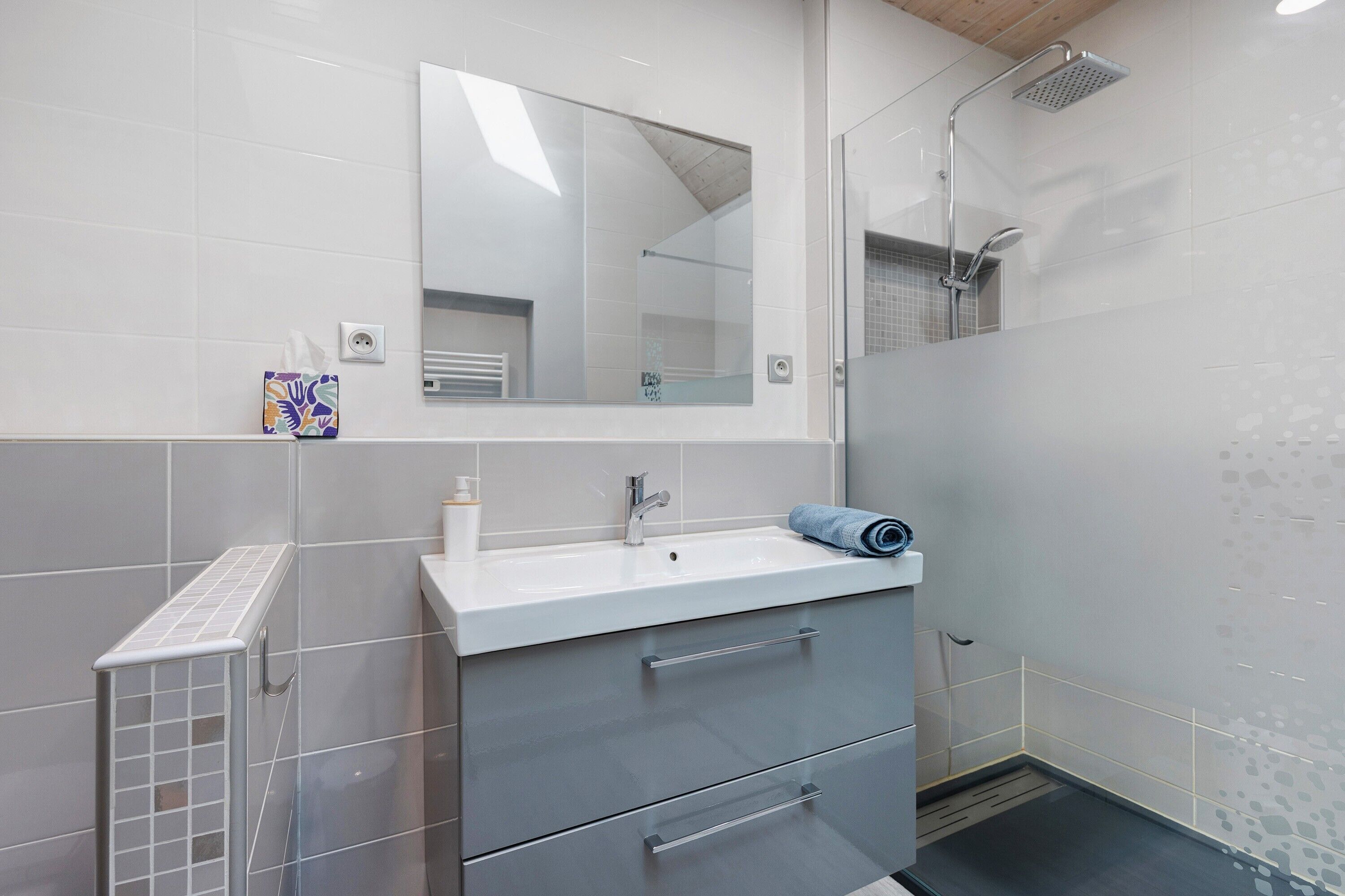 Une salle de bain moderne avec un lavabo blanc, un miroir et une douche.