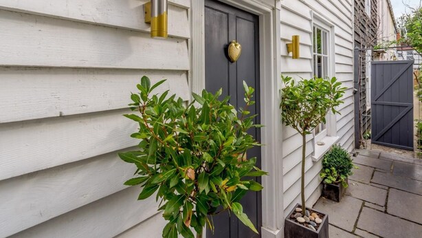 Een huis met witte bekleding, een donkere voordeur en twee kleine plantenpotten op het terras.