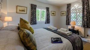 Een slaapkamer met een groot bed, twee nachtkastjes, een raam met gordijnen en ingelijste foto’s aan de muur.