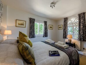 A bedroom with a large bed, two bedside tables, a window with curtains, and framed pictures on the wall. - 1 Bed in Brockenhurst (oc-78767) (Bucklers Hard)