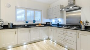 Een moderne keuken met witte kastjes, een roestvrijstalen afzuigkap en een raam met zonwering.