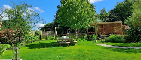 A well-maintained garden with a swing set, picnic table, and pergola.