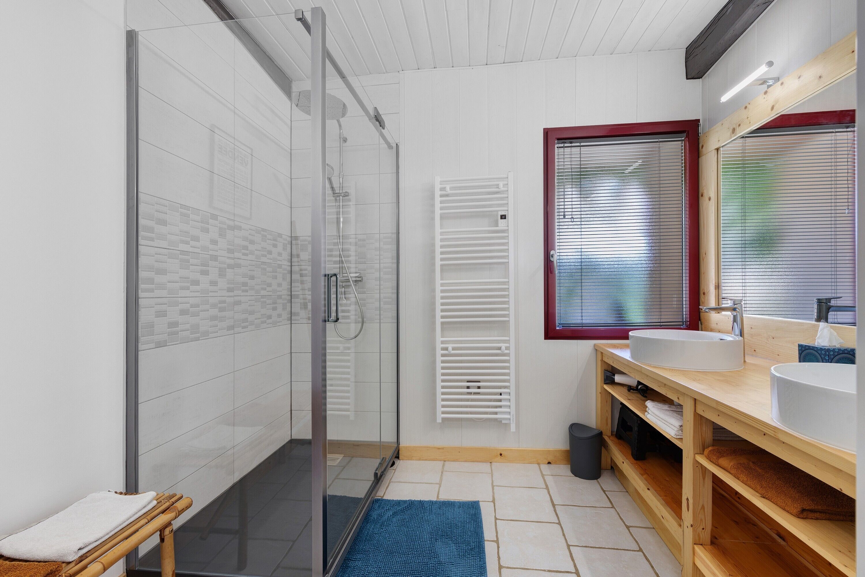 Une salle de bain moderne avec une douche à parois de verre, un meuble-lavabo en bois et une fenêtre équipée de stores.