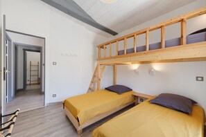 Ein Zimmer mit einem Etagenbett, zwei Einzelbetten, einer Leiter und einer Tür zu einem weiteren Raum.