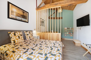 A bedroom with a bed, a mounted television, a bookshelf, and a wooden partition.