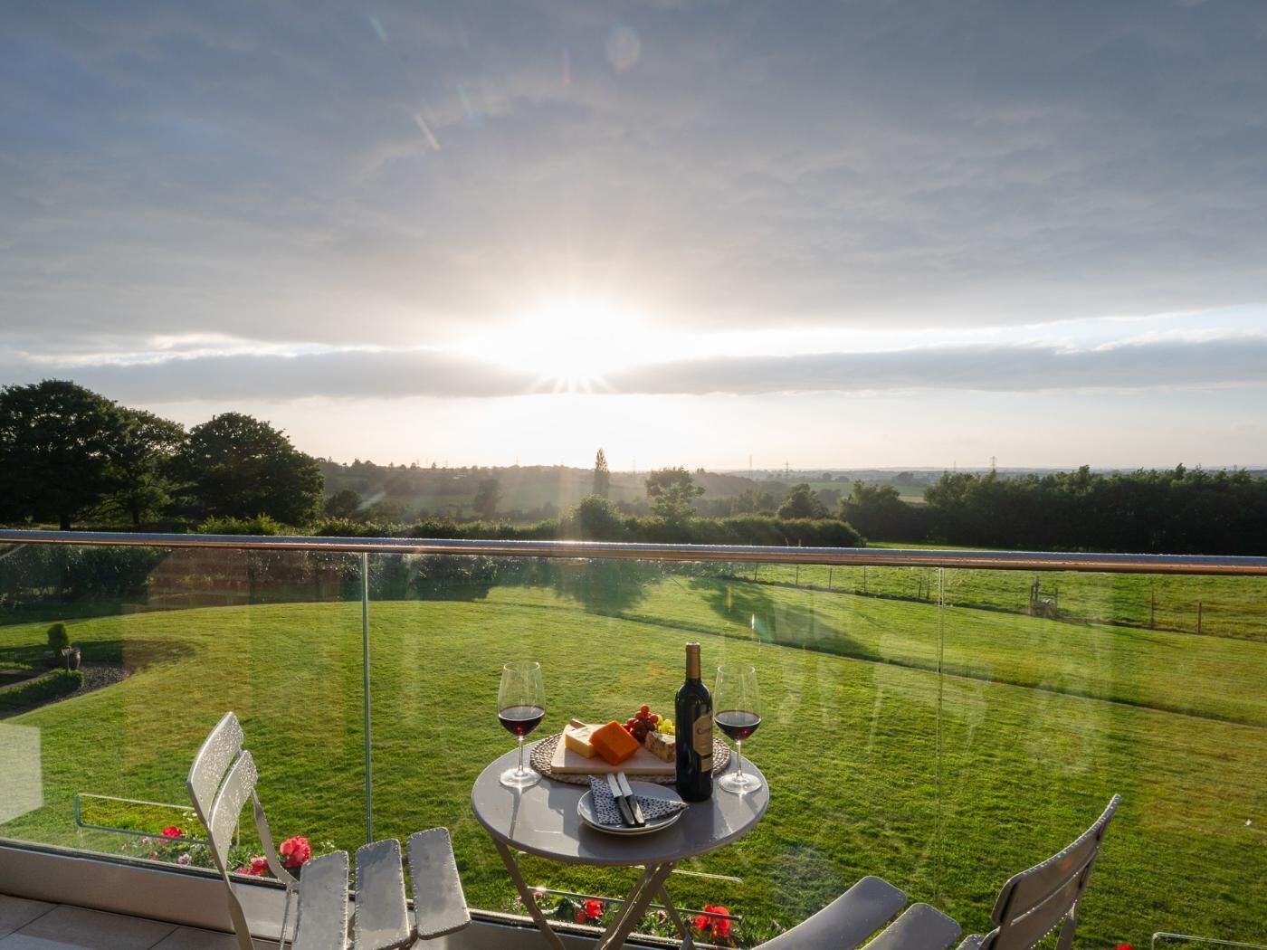 Eine Terrasse mit Tisch für zwei Personen, Blick auf ein Wiesenfeld und eine entfernte Landschaft.