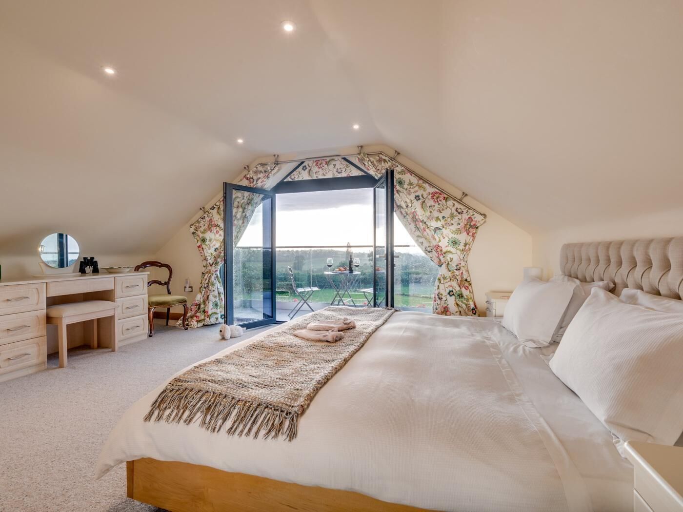 A bedroom with a large bed, a desk, and a chair, with a view of the outdoors.