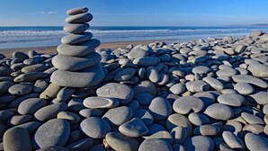 Ein Strand mit einem Stapel glatter, runder Steine im Vordergrund und einem ruhigen Meer im Hintergrund.