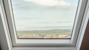 Ein Dachfenster mit Blick auf eine ländliche Landschaft, darunter Felder und ferne Hügel.