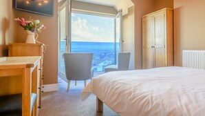 Ein Schlafzimmer mit Bett, Schreibtisch, Stuhl, Kleiderschrank und einem großen Fenster mit Aussicht.