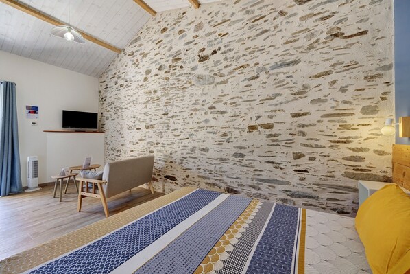 A room with a stone wall, a flat-screen TV mounted on the wall, a sofa, a small table with a chair, and a patterned rug.