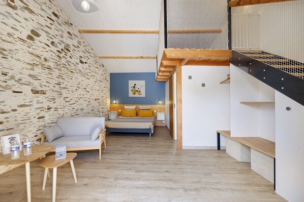 A modern interior with a stone wall, a blue accent wall, a bed with yellow pillows, a wooden bench, and a staircase with a netted railing.