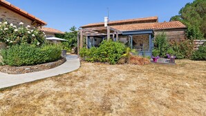 Ein Wohnhaus mit Steinmauer, Holzpergola und Garten mit verschiedenen Pflanzen.