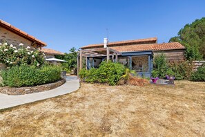 Una propiedad residencial con un muro de piedra, una pérgola de madera y un jardín con diversas plantas.