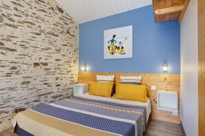 A bedroom with a stone wall, a bed with patterned bedding, a wooden headboard, and a wall-mounted poster.