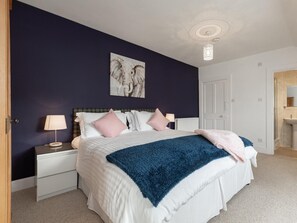 Ein Schlafzimmer mit einem Bett, Nachttischen, einer Lampe, einem Gemälde und einer Tür.