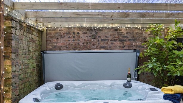 A hot tub with a wooden headboard, surrounded by a brick wall and string lights. - 5 Bed in Melrose (oc-79418) (Melrose)