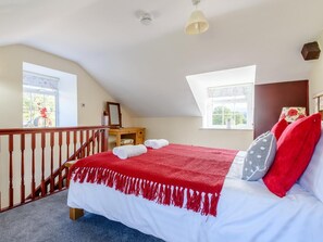 A bedroom with a sloped ceiling, two windows, a bed with a red blanket, a wooden dresser, and a staircase. - 1 Bed in Conwy (oc-79357) (Ty'n-y-groes)