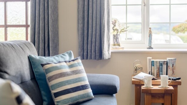 Ein Zimmer mit einer Couch, einem kleinen Tisch mit Büchern und einer Figur, sowie einem Fenster mit Vorhängen.