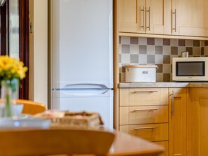 A kitchen with wooden cabinets, a white refrigerator, a microwave, and a bread box on the countertop. - 1 Bed in Conwy (oc-79357) (Ty'n-y-groes)