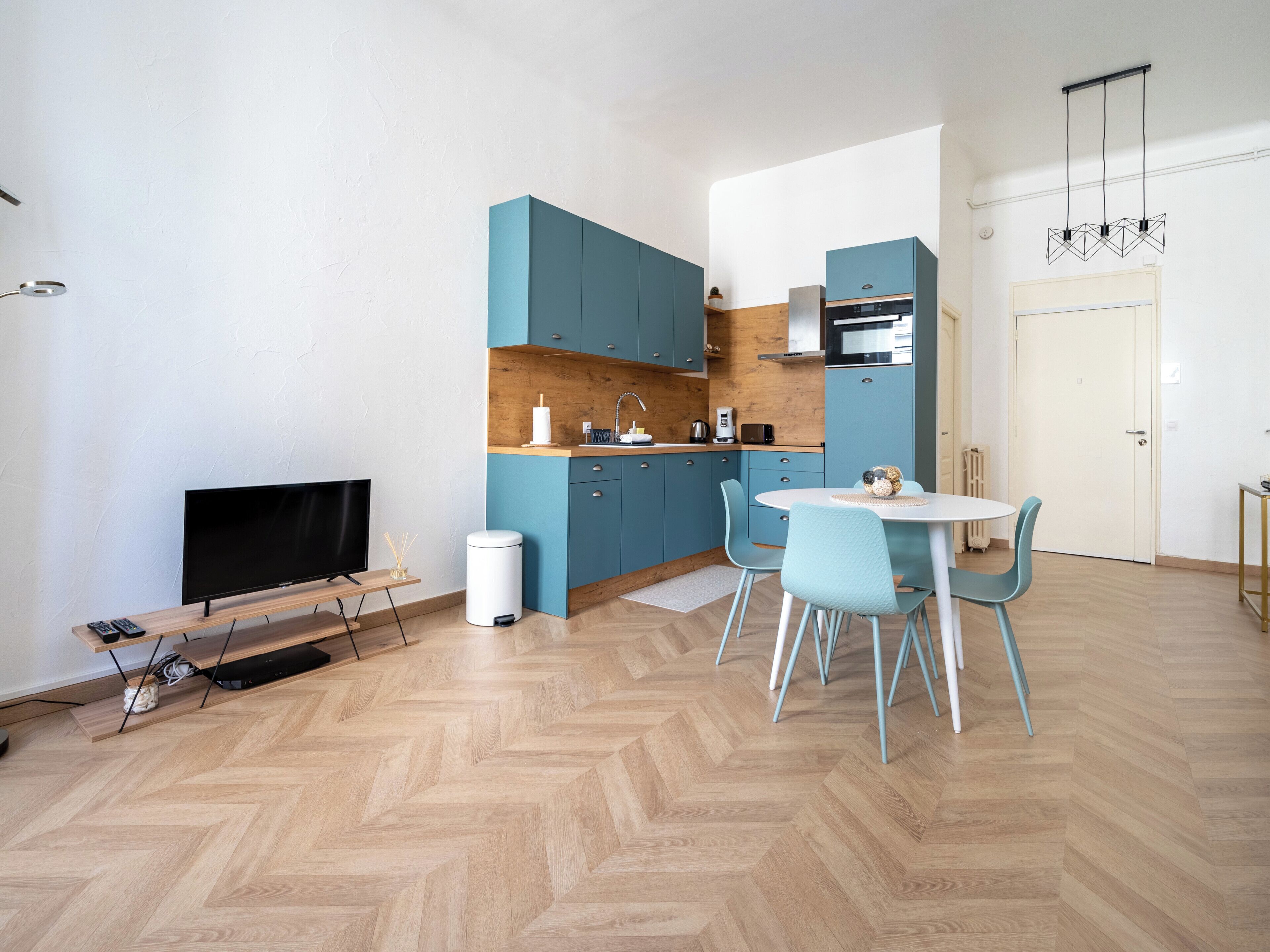 Una cucina moderna con mobili blu, un tavolo da pranzo con sedie, una televisione e un cestino.