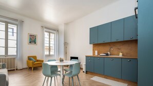 A modern kitchen with blue cabinets, a white dining table with chairs, a radiator, and a window with curtains. - Spacious and Bright, Near Train Station and Palais des Festivals - BENAKEY (Cannes)