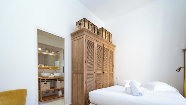 A bedroom with a bed, a wooden wardrobe, a yellow chair, and a bathroom with a mirror and sink. - Spacious and Bright, Near Train Station and Palais des Festivals - BENAKEY (Cannes)