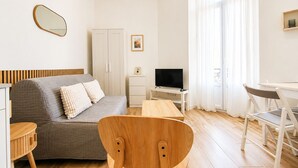 Un soggiorno moderno con un divano, una sedia di legno, una TV, una scrivania e un'armadio.