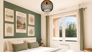 A bedroom with a bed, a nightstand, a lamp, a window with curtains, and wall art. - Sunny Terrace & Open Views | Pool, Parking, A/C | Cannes – BENAKEY (Cannes)