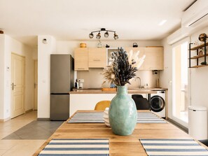 Una cocina moderna con armarios de madera, un refrigerador de acero inoxidable, una lavadora y un jarrón con flores secas sobre la mesa de comedor.