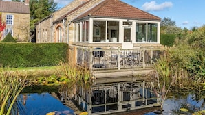 Ein Steinhaus mit einem Ziegeldach, einer Veranda und einem Teich davor.