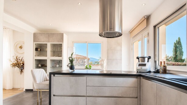 Een moderne keuken met een groot eiland, inbouwplanken en uitzicht op de omgeving.