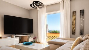 Een moderne woonkamer met een flatscreen televisie, een witte salontafel, beige banken en uitzicht op een balkon.