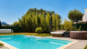 Een rechthoekig zwembad met een houten terras eromheen, een jacuzzi en een overdekte zithoek.
