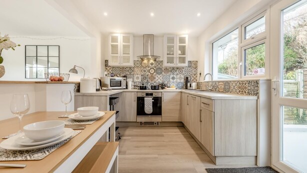 A modern kitchen with light wood cabinets, a microwave, oven, and a dining area with a table set for two. - 2 Bed in Wareham (oc-79228) (West Lulworth)
